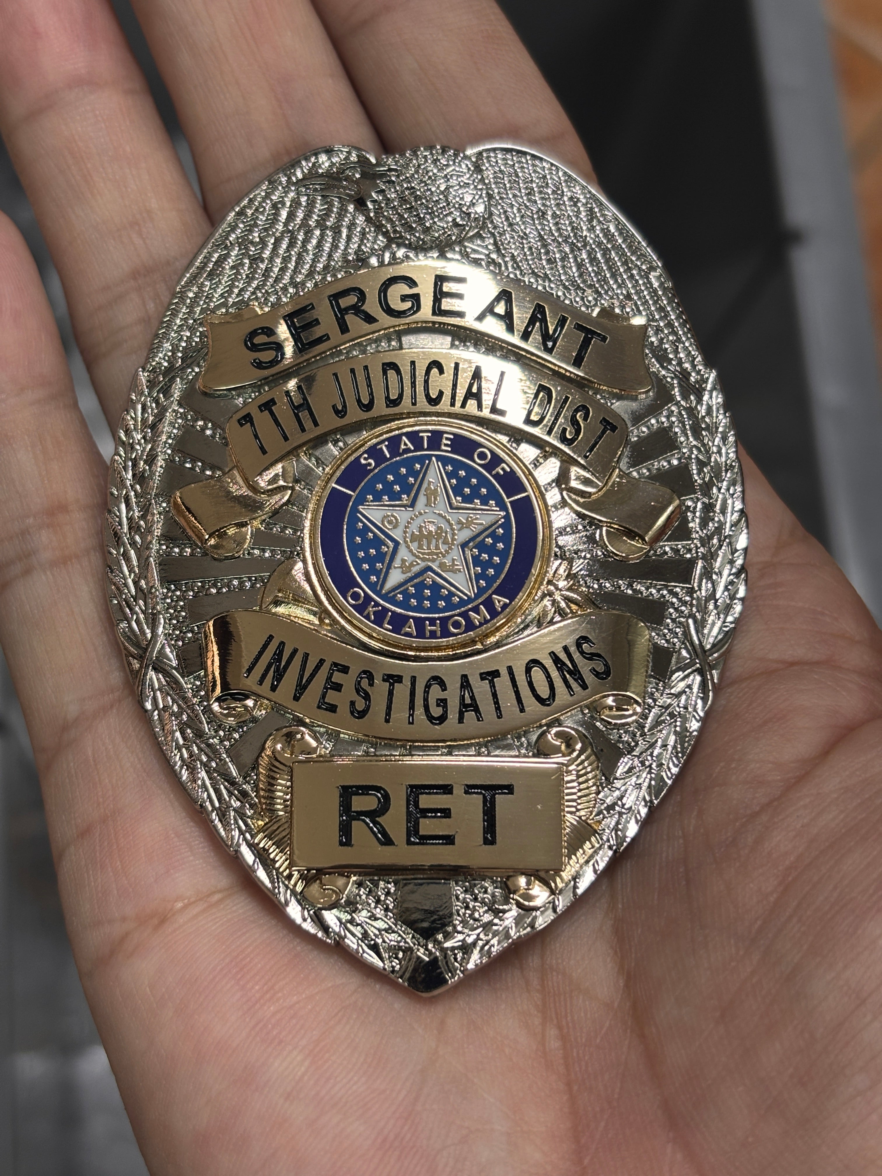 Two-tone silver-and-gold custom investigations badge with eagle crest, black lettering, Oklahoma center seal, and RET nameplate