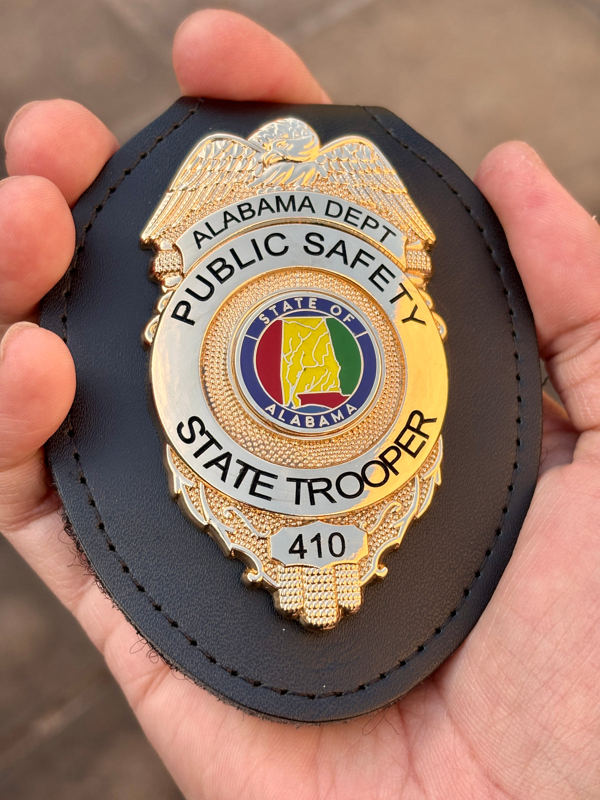 Two-tone gold-and-silver state trooper-style badge in a black leather holder with eagle crest, Alabama-themed center emblem, Public Safety lettering, and number 410