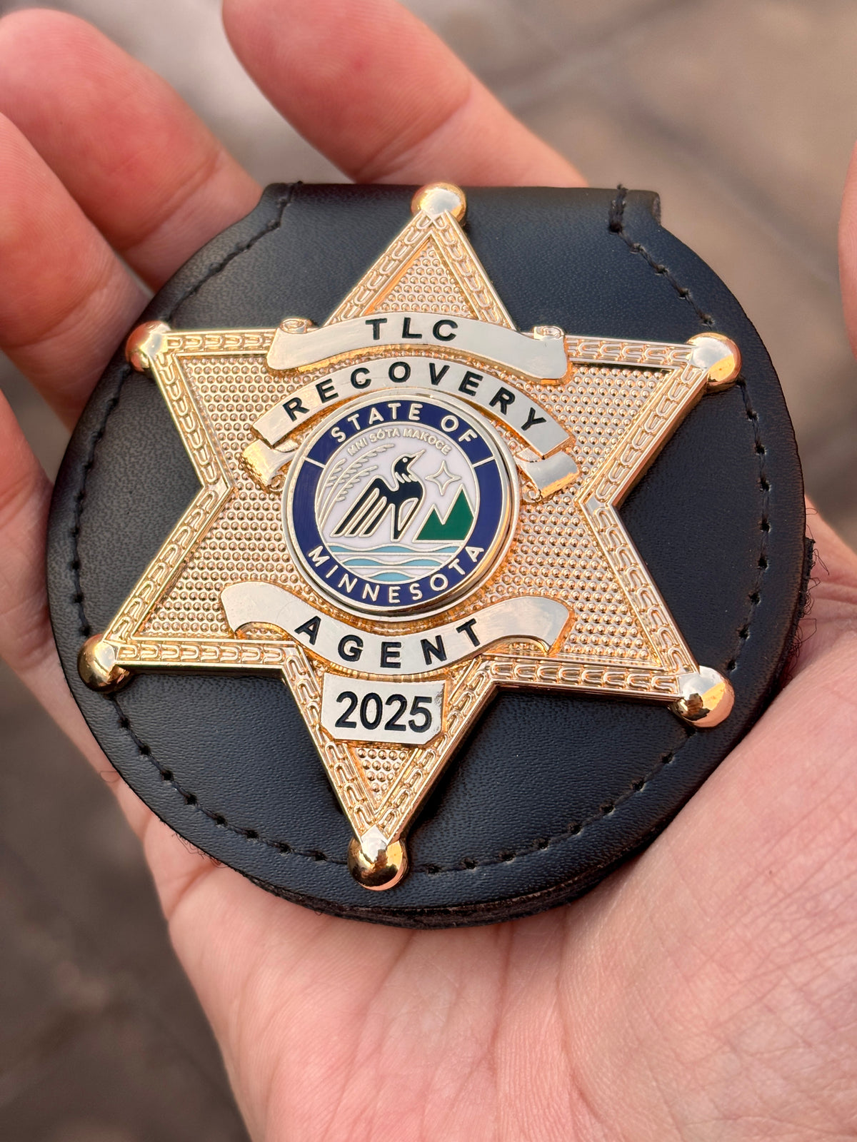 Gold-tone six-point RECOVERY AGENT star badge in a black leather holder, with TLC top banner, Minnesota-themed center emblem, and 2025 lower panel