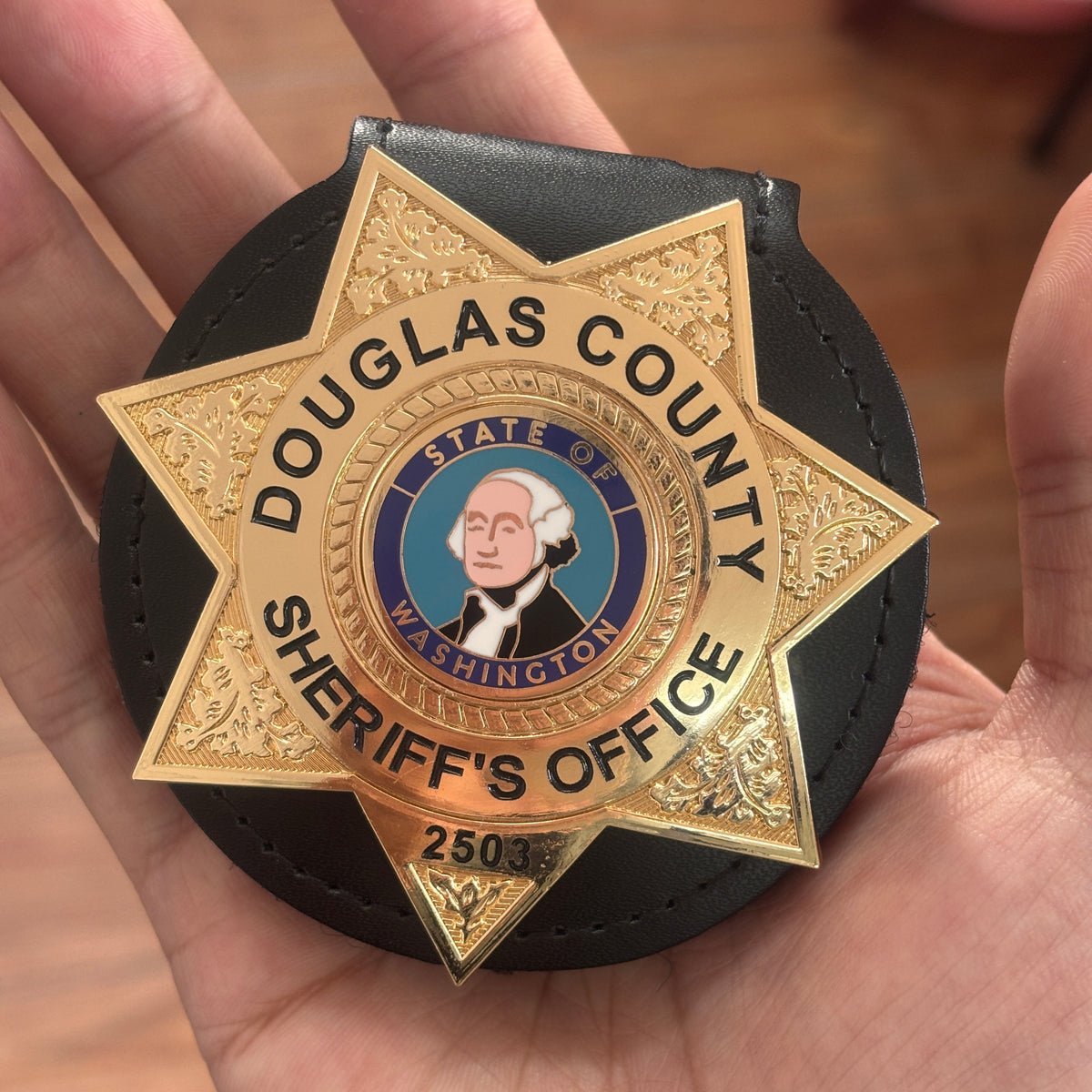 Gold-tone six-point sheriff star badge in a black leather holder with black county lettering, Washington-themed portrait center emblem, office title, and number 2503
