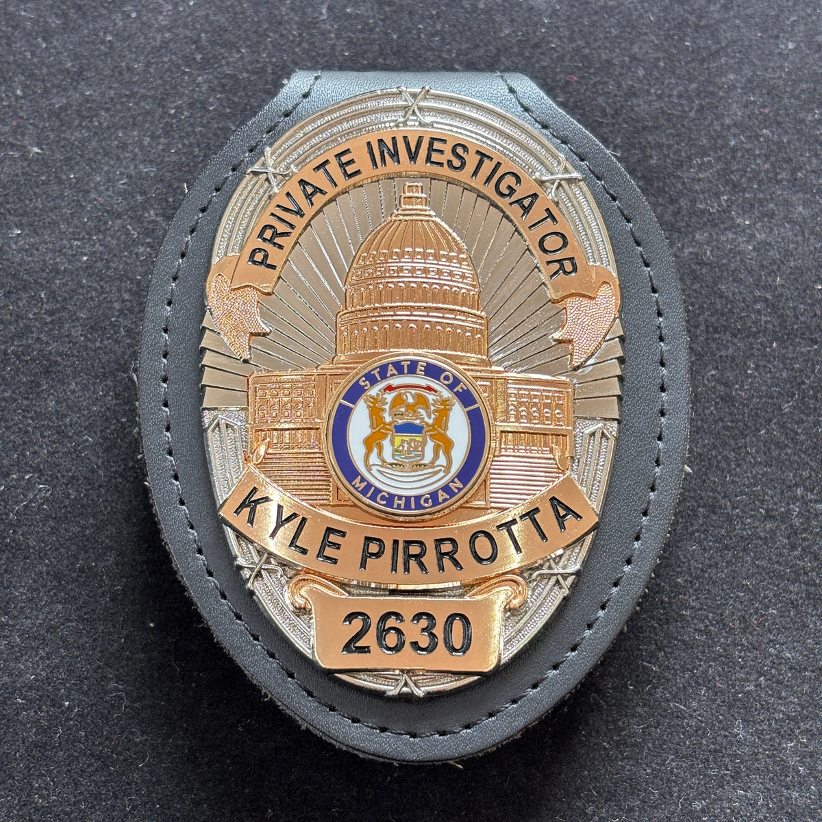 Two-tone personalized private investigator badge with a domed civic emblem, black lettering, identification number, and black leather holder