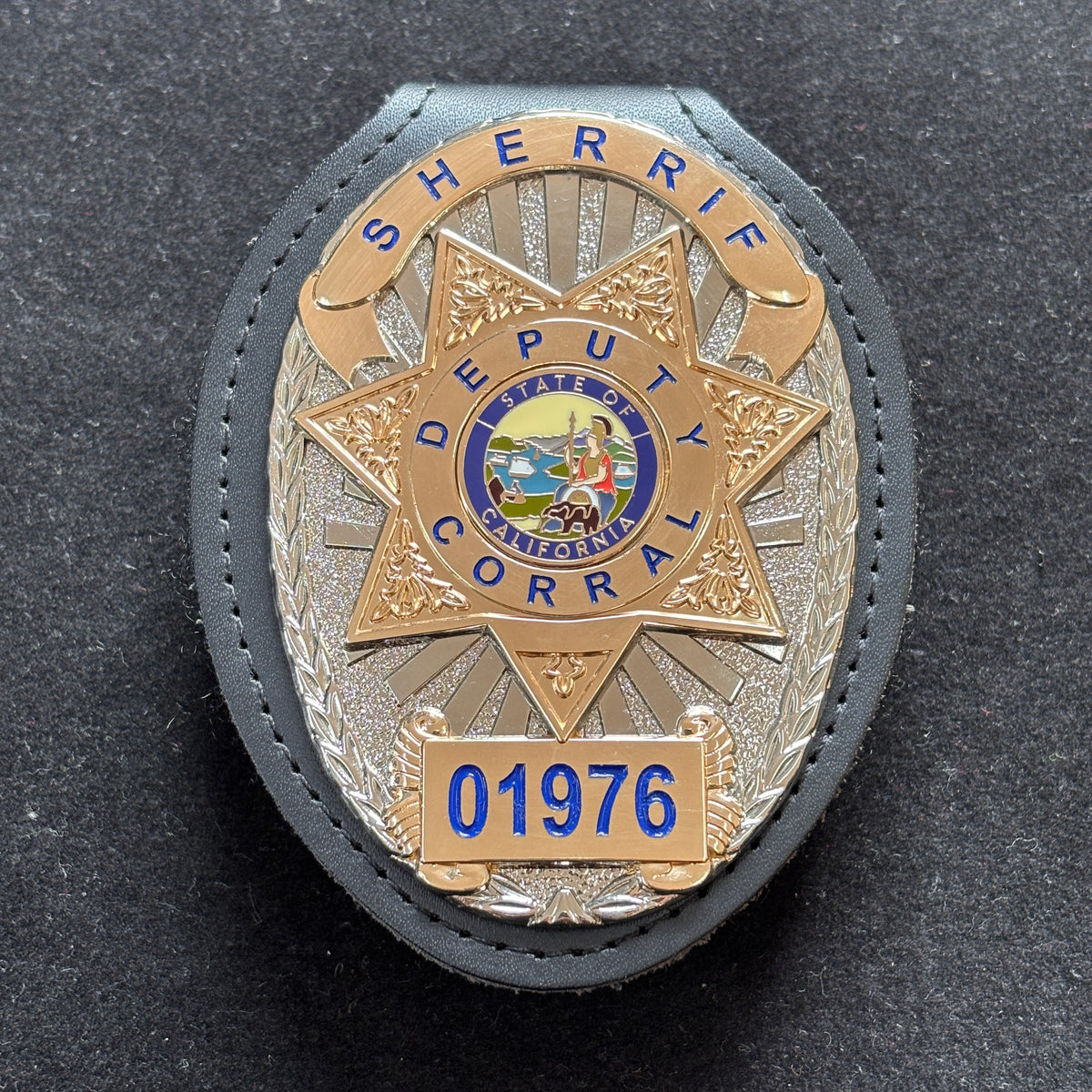 Two-tone sheriff-style custom badge with a gold seven-point star, silver oval background, blue lettering, colored California-themed center emblem, number panel, and black leather holder