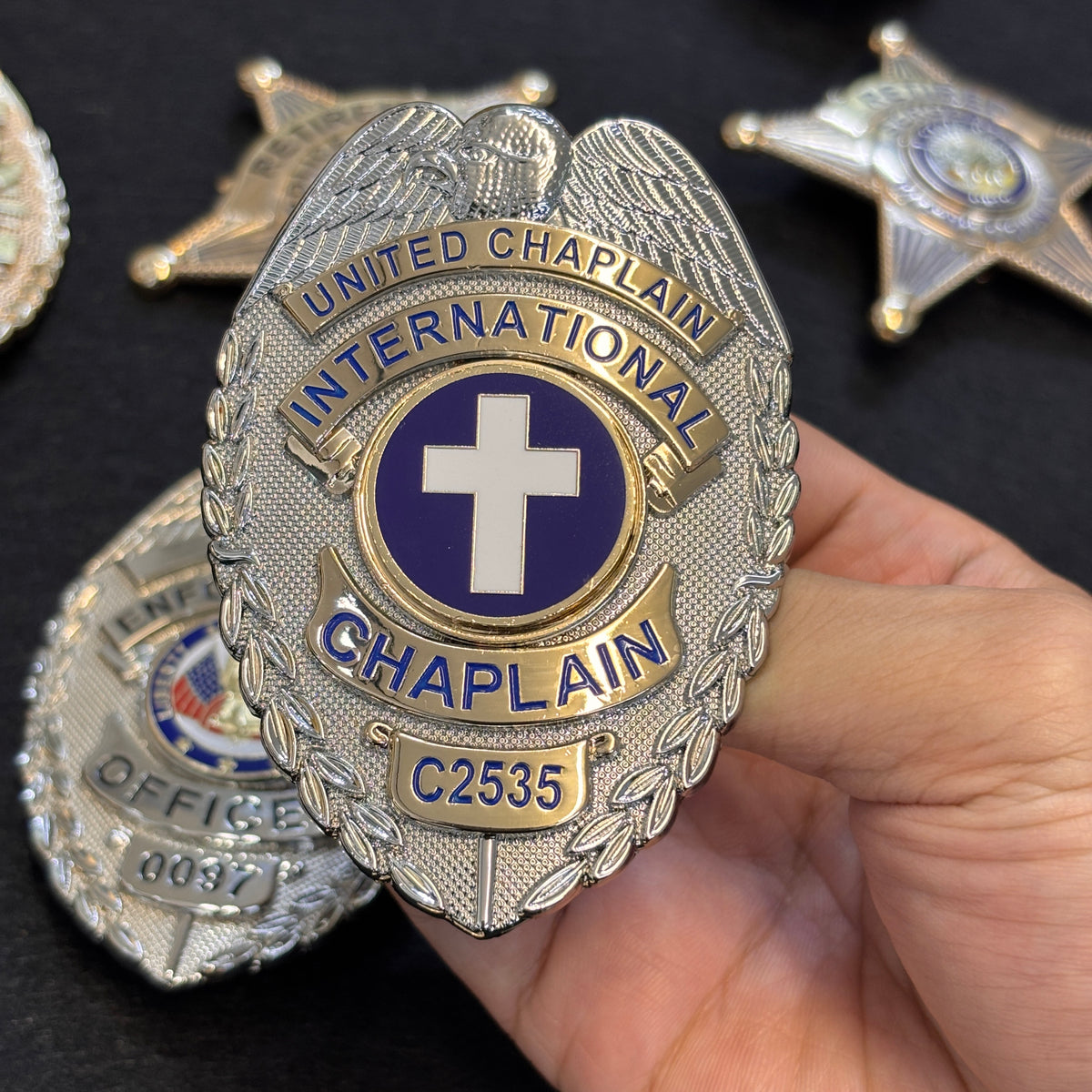 Two-tone oval UNITED CHAPLAIN INTERNATIONAL badge with silver eagle, gold banners, blue lettering, purple-and-white cross emblem, CHAPLAIN title, and identifier C2535