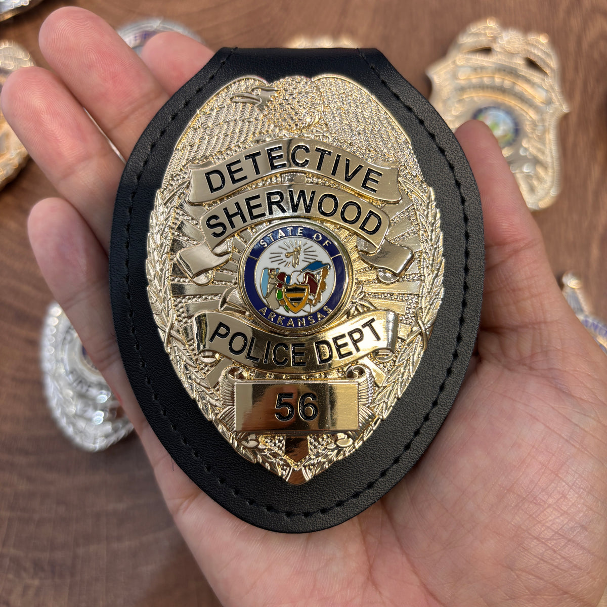 Gold-tone eagle-top detective badge in a black holder, with SHERWOOD, Arkansas state emblem, POLICE DEPT, and number 56