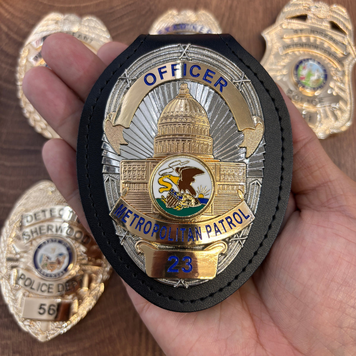Two-tone gold-and-silver metropolitan patrol officer badge with blue lettering, detailed civic emblem, number 23, displayed in a black leather badge holder