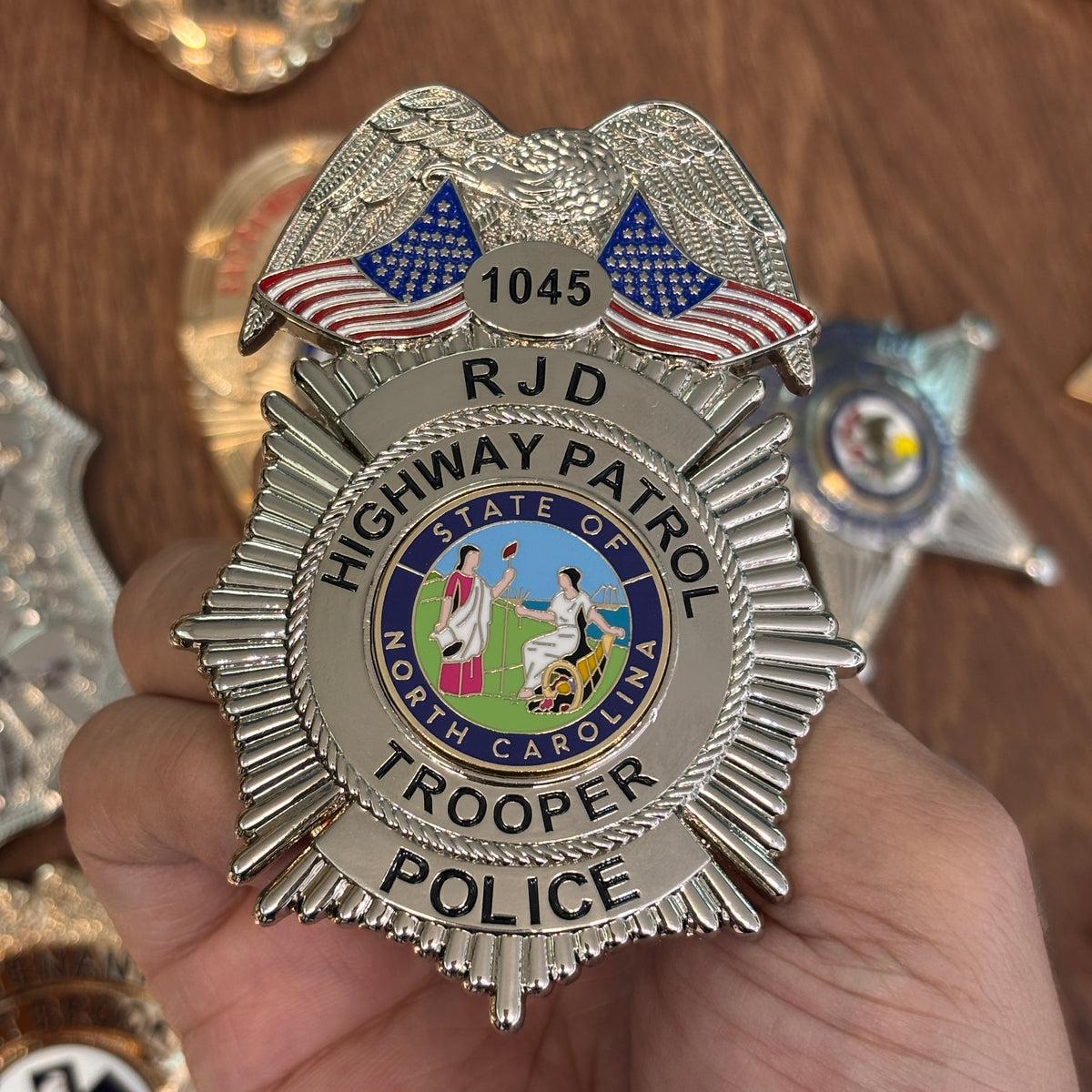 Silver-tone Highway Patrol trooper-style badge with eagle crest, two American flags, RJD initials, North Carolina state emblem, POLICE title, and number 1045