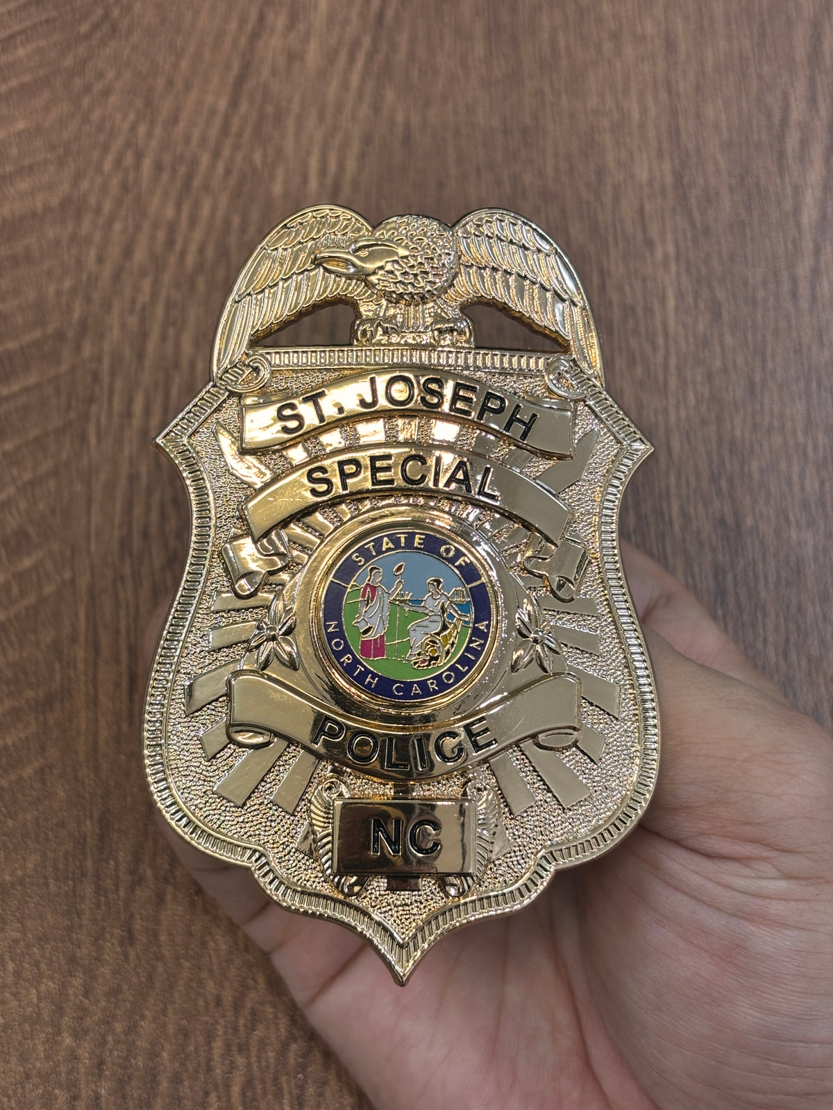 Gold-tone shield-shaped special police-style custom badge with eagle crest, black lettering, North Carolina-themed center emblem, textured field, and lower location panel