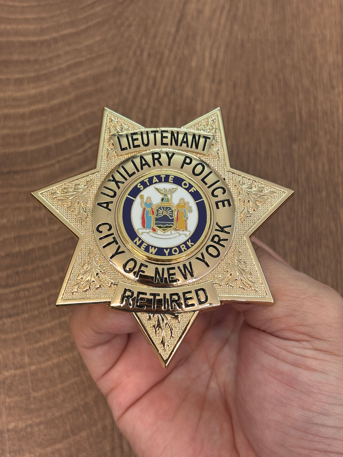 Six-point gold-tone police-style custom badge with black lettering, textured rays, colored center emblem, rank panel, and lower status banner